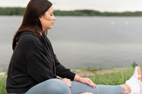 Woman meditating outdoors by a tranquil lakeside, fostering health and wellness.